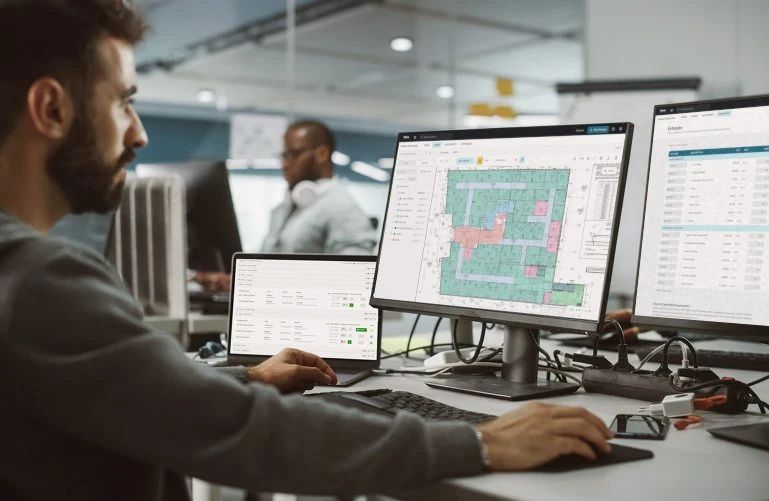 Estimator reviewing a room takeoff and its estimate worksheet in Yanno on two monitors